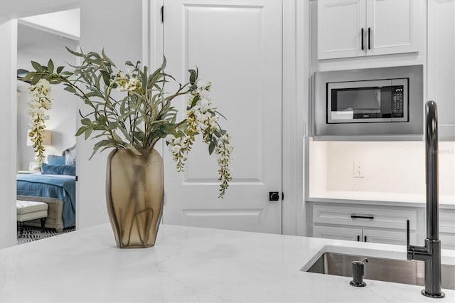 room details featuring white cabinets, stainless steel microwave, sink, and light stone counters