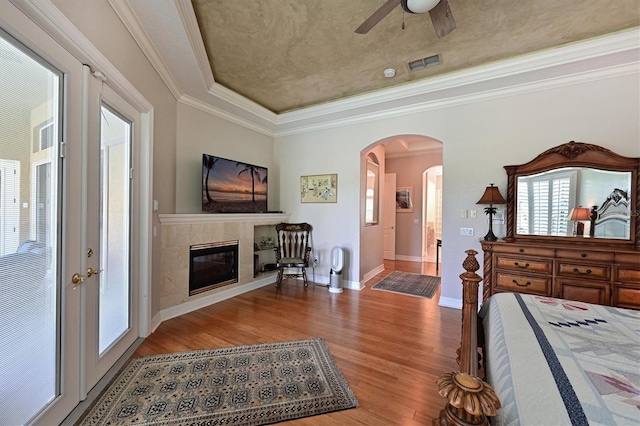 bedroom featuring french doors, crown molding, ceiling fan, a premium fireplace, and light hardwood / wood-style floors