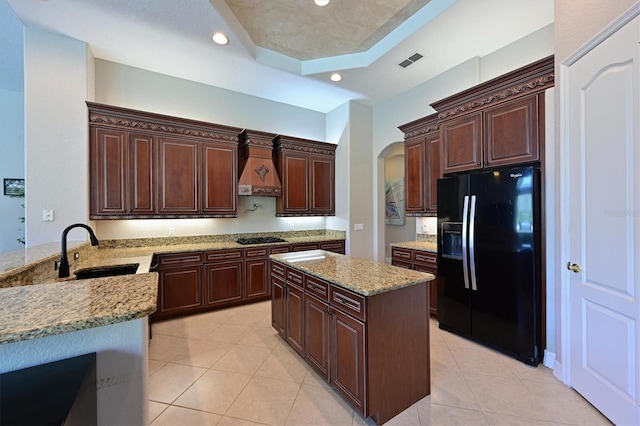 kitchen featuring stainless steel gas stovetop, a raised ceiling, sink, light stone counters, and black fridge with ice dispenser