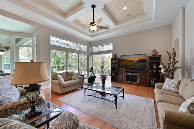 living room with ceiling fan, a healthy amount of sunlight, light wood-type flooring, and coffered ceiling