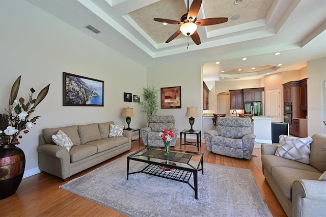 living room featuring a tray ceiling, ceiling fan, and light hardwood / wood-style floors