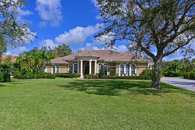 mediterranean / spanish house with stucco siding, a tiled roof, and a front yard