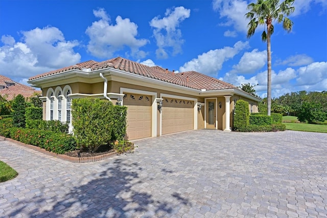 mediterranean / spanish-style house with a tile roof, decorative driveway, a garage, and stucco siding