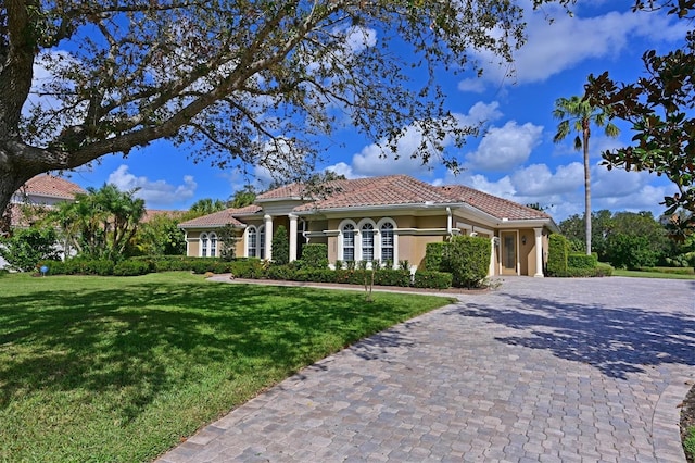 mediterranean / spanish-style home featuring decorative driveway, stucco siding, a front yard, and a tile roof