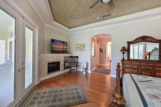 bedroom with visible vents, wood finished floors, a high end fireplace, arched walkways, and crown molding