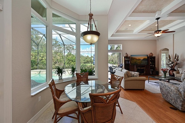 dining space featuring light wood-type flooring, beamed ceiling, coffered ceiling, arched walkways, and baseboards