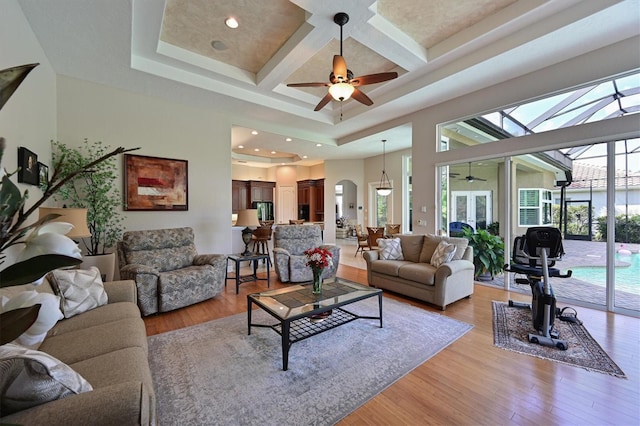 living area with beam ceiling, light wood-style flooring, coffered ceiling, a high ceiling, and ceiling fan