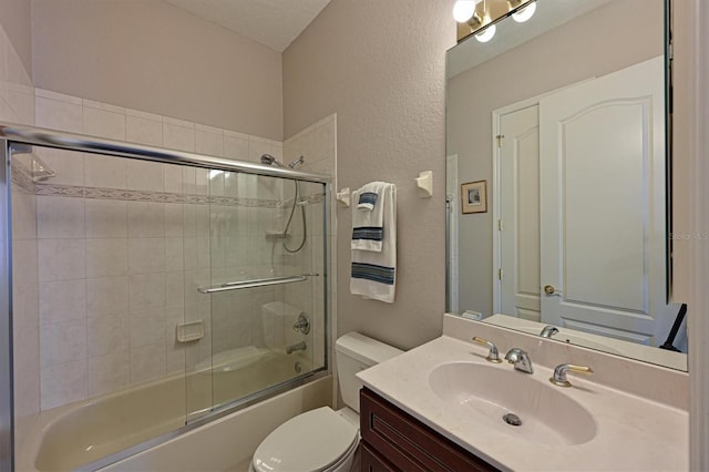 bathroom featuring a textured wall, bath / shower combo with glass door, vanity, and toilet