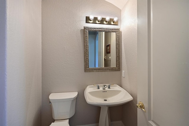 half bathroom with toilet and a textured wall