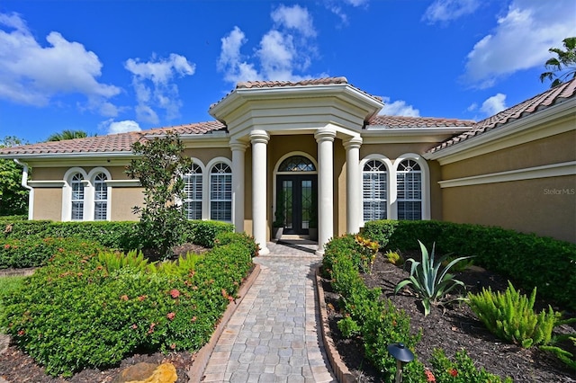 property entrance featuring a tile roof, french doors, and stucco siding