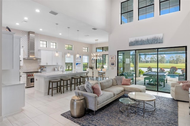 tiled living room featuring a high ceiling, sink, a healthy amount of sunlight, and a notable chandelier