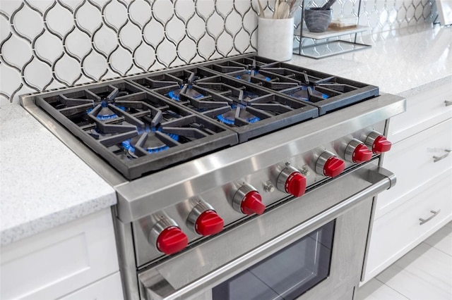 room details with decorative backsplash, white cabinetry, stainless steel stove, and light stone counters