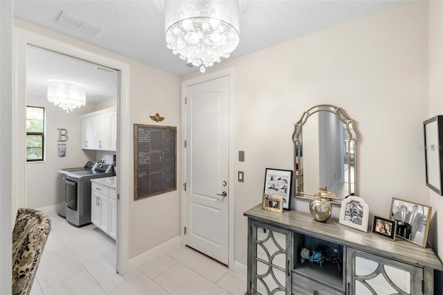 tiled entryway featuring washing machine and dryer and an inviting chandelier