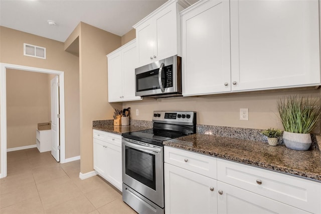 kitchen featuring light tile patterned flooring, white cabinetry, appliances with stainless steel finishes, and dark stone counters