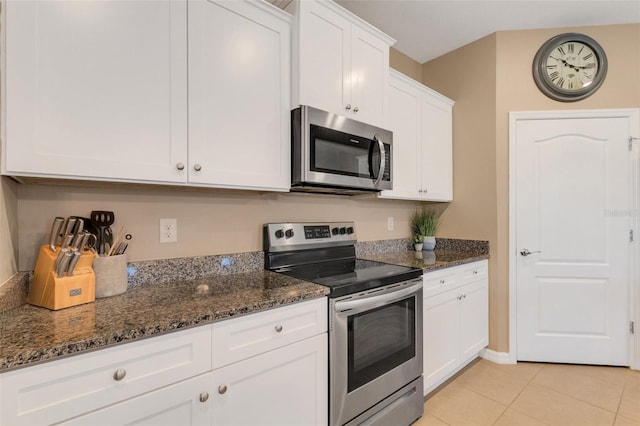 kitchen featuring light tile patterned floors, white cabinetry, appliances with stainless steel finishes, and dark stone counters