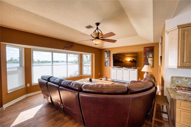 living room with dark wood-type flooring, a textured ceiling, ceiling fan, and a raised ceiling