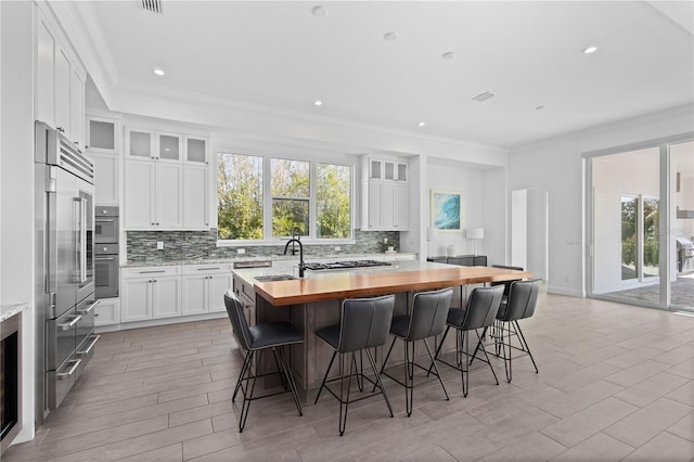 kitchen with a kitchen island with sink, decorative backsplash, white cabinetry, and a breakfast bar