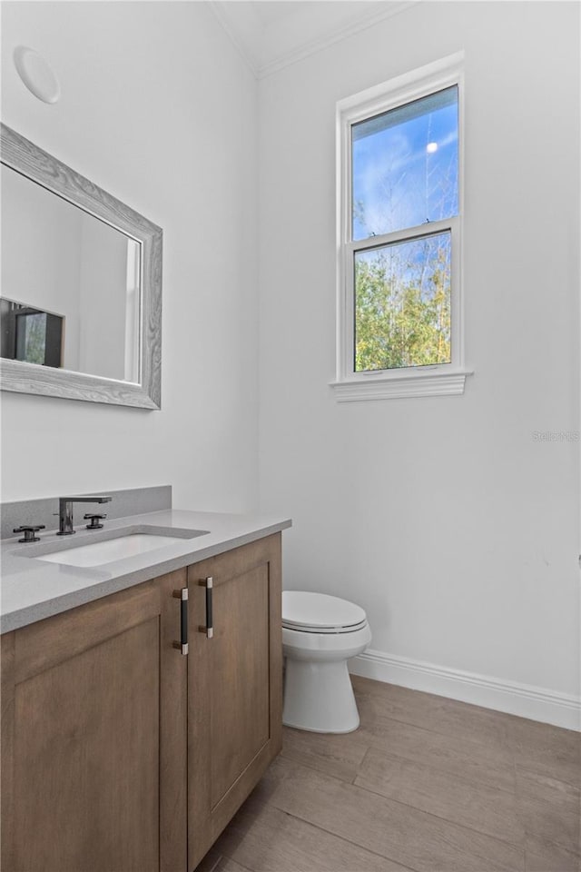 bathroom with toilet, vanity, wood-type flooring, and ornamental molding