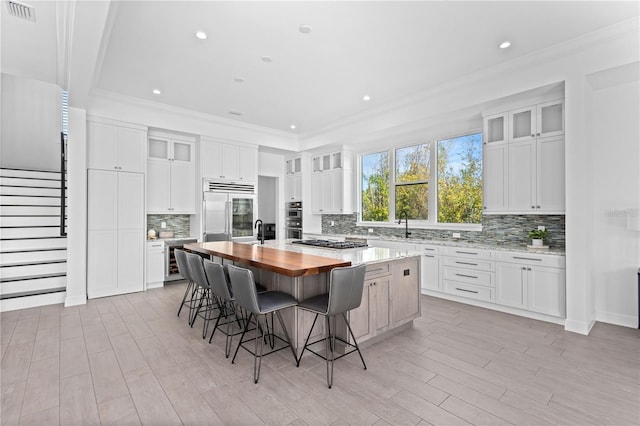 kitchen featuring a large island, appliances with stainless steel finishes, white cabinetry, and butcher block countertops