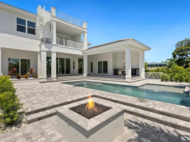 rear view of house featuring a patio area, a fire pit, pool water feature, and a balcony