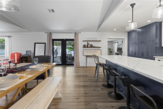 kitchen featuring dark hardwood / wood-style flooring, wooden walls, pendant lighting, and light stone counters