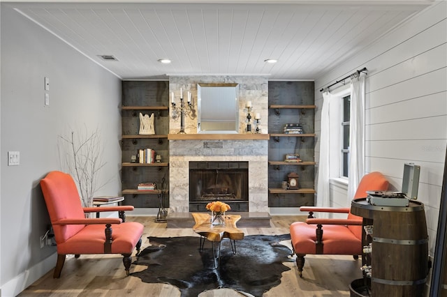 living area featuring wooden ceiling, built in shelves, a large fireplace, wood-type flooring, and wooden walls