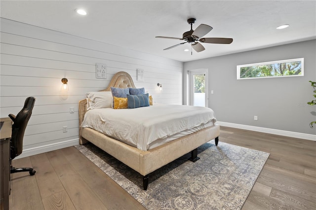 bedroom with hardwood / wood-style floors, ceiling fan, and wood walls