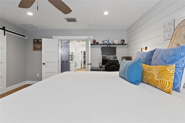 bedroom featuring hardwood / wood-style flooring, a barn door, and ceiling fan