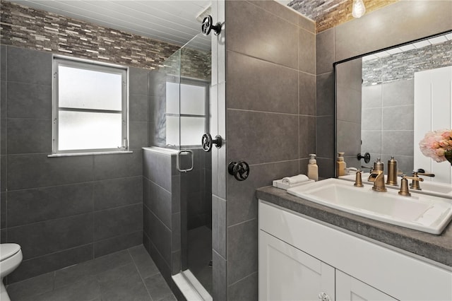 bathroom with vanity, a shower with shower door, tile patterned floors, toilet, and tile walls