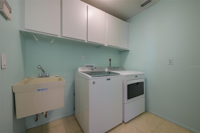 laundry room with washing machine and clothes dryer, sink, cabinets, a textured ceiling, and light tile patterned floors