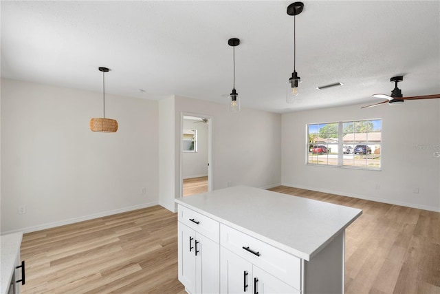 kitchen with white cabinets, light wood-type flooring, hanging light fixtures, and ceiling fan