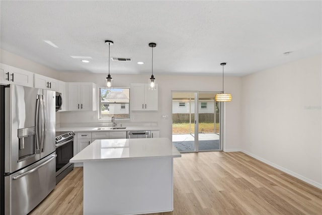 kitchen with pendant lighting, stainless steel appliances, white cabinetry, and light hardwood / wood-style flooring