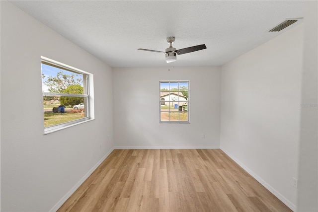 empty room featuring a wealth of natural light, a textured ceiling, and light wood-type flooring