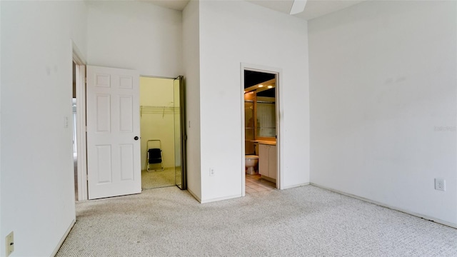 unfurnished bedroom with a spacious closet, light carpet, ensuite bath, and a closet