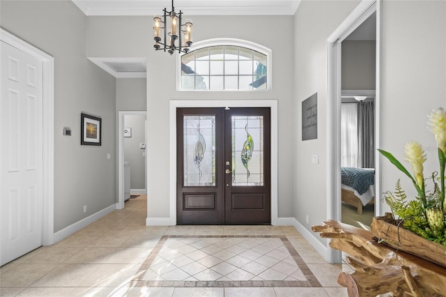 foyer entrance featuring baseboards, an inviting chandelier, a high ceiling, crown molding, and french doors