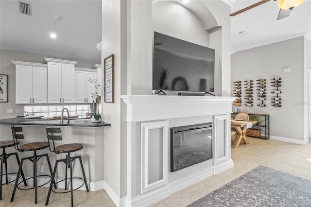 kitchen featuring a kitchen breakfast bar, white cabinets, decorative backsplash, dark countertops, and a glass covered fireplace