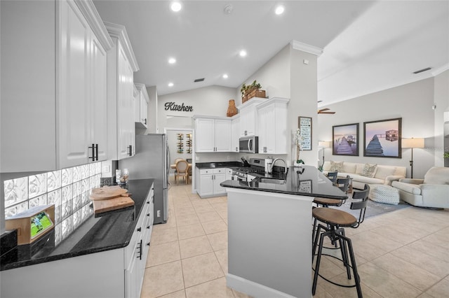 kitchen with light tile patterned floors, appliances with stainless steel finishes, open floor plan, white cabinetry, and a peninsula