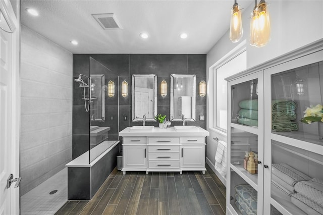 bathroom featuring double vanity, visible vents, wood tiled floor, walk in shower, and a sink