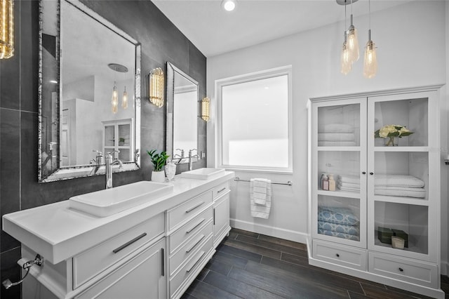 bathroom with wood finish floors, a sink, baseboards, and double vanity