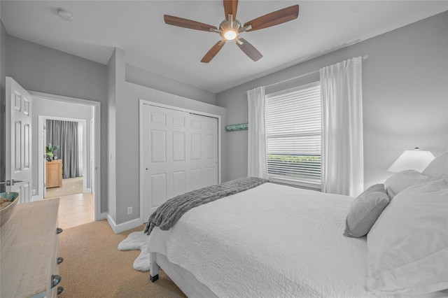 bedroom with light carpet, ceiling fan, baseboards, and a closet