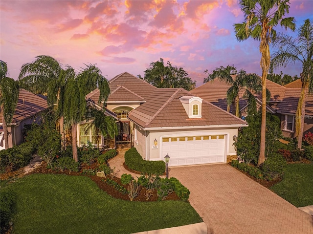 mediterranean / spanish-style home featuring decorative driveway, stucco siding, an attached garage, a tiled roof, and a front lawn