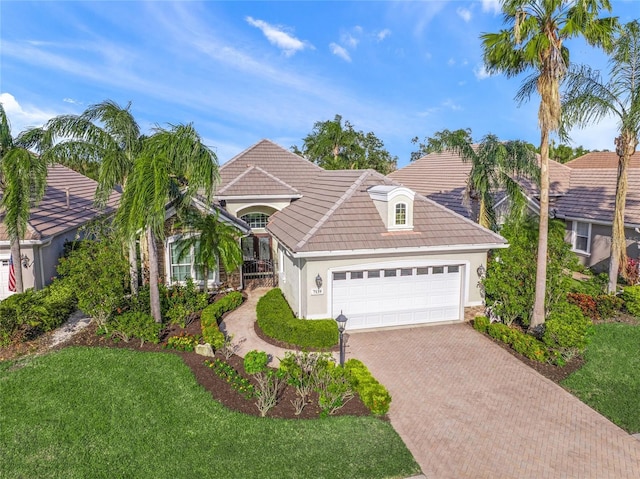 view of front of property with an attached garage, a tiled roof, decorative driveway, stucco siding, and a front yard