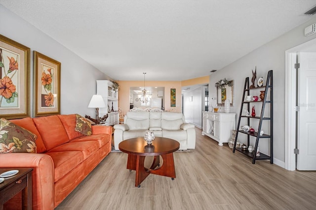 living room featuring an inviting chandelier, a textured ceiling, and light hardwood / wood-style floors