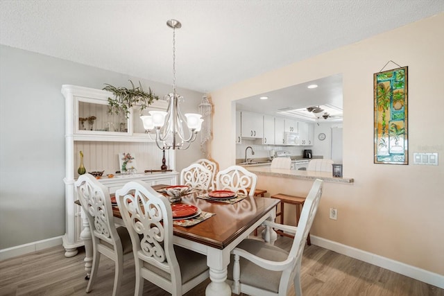 dining space featuring sink, a textured ceiling, light hardwood / wood-style floors, and a chandelier