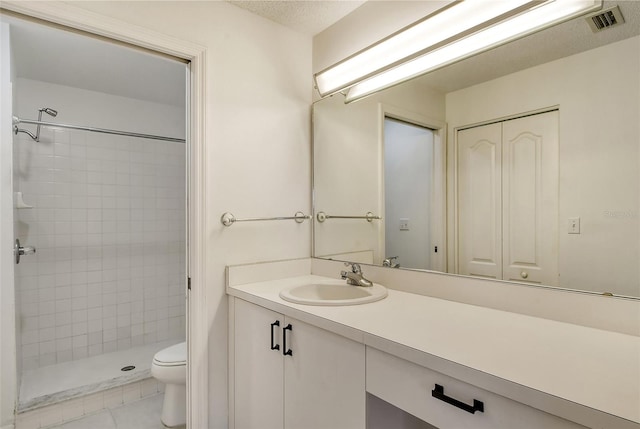 bathroom with toilet, vanity, tile patterned floors, and tiled shower