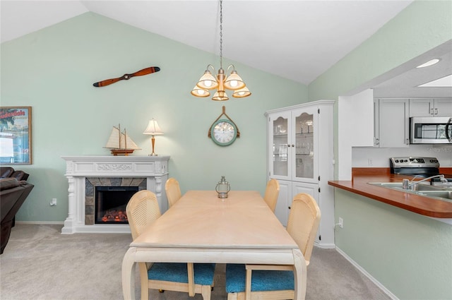 carpeted dining room with a stone fireplace, vaulted ceiling, and a notable chandelier