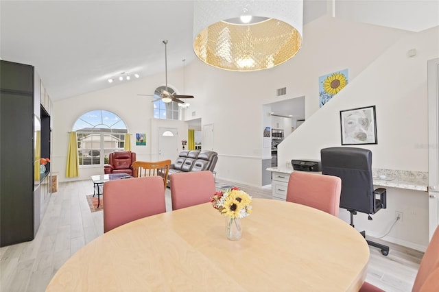 dining area with built in desk, ceiling fan, light wood-type flooring, and high vaulted ceiling