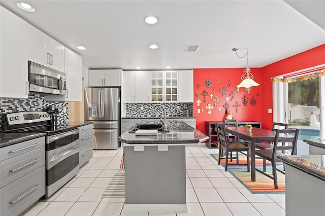 kitchen with stainless steel appliances, white cabinetry, sink, decorative light fixtures, and a kitchen island with sink