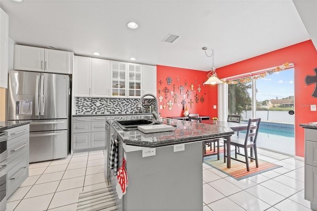 kitchen with a center island with sink, sink, decorative light fixtures, white cabinets, and stainless steel fridge