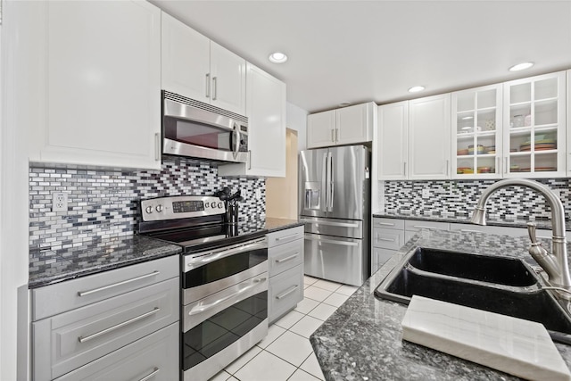 kitchen with light tile patterned flooring, stainless steel appliances, backsplash, sink, and white cabinets